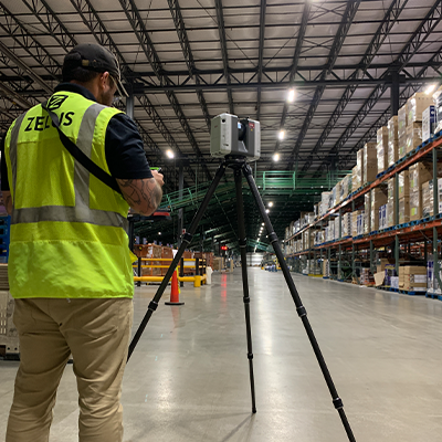 ZELUS technician using a 3D laser scanner in a warehouse to capture floor flatness data.