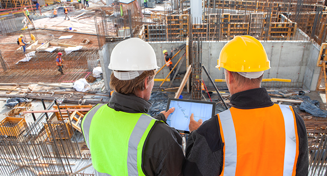 Construction professionals reviewing BIM coordination plans on a tablet at an active job site
