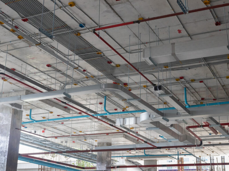 Installed MEP systems in a commercial building showing overhead ductwork, piping, and cable tray coordination