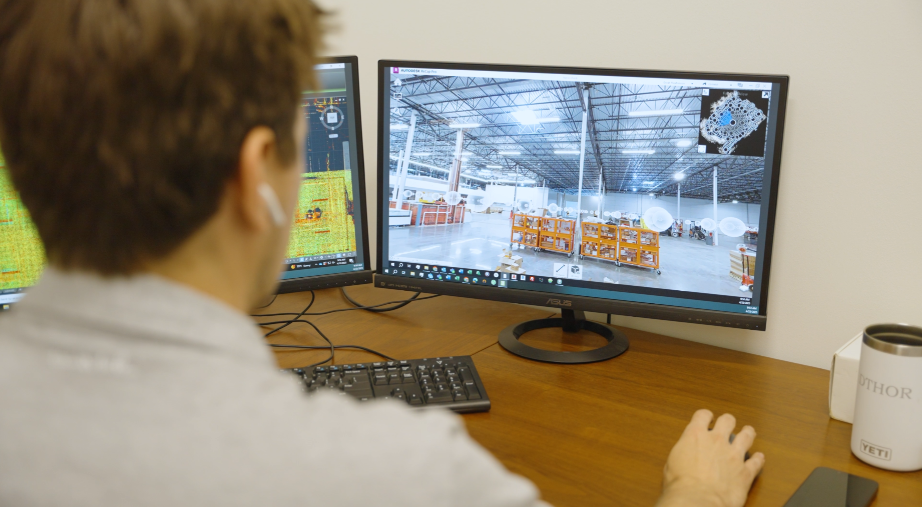 Man sits at desk looking at computer screens with  a point cloud and 3D tour viewer on them