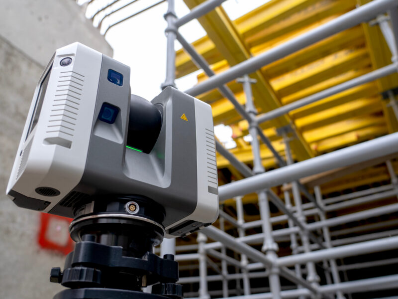 3D laser scanner positioned on an active construction site near scaffolding and concrete structural elements.