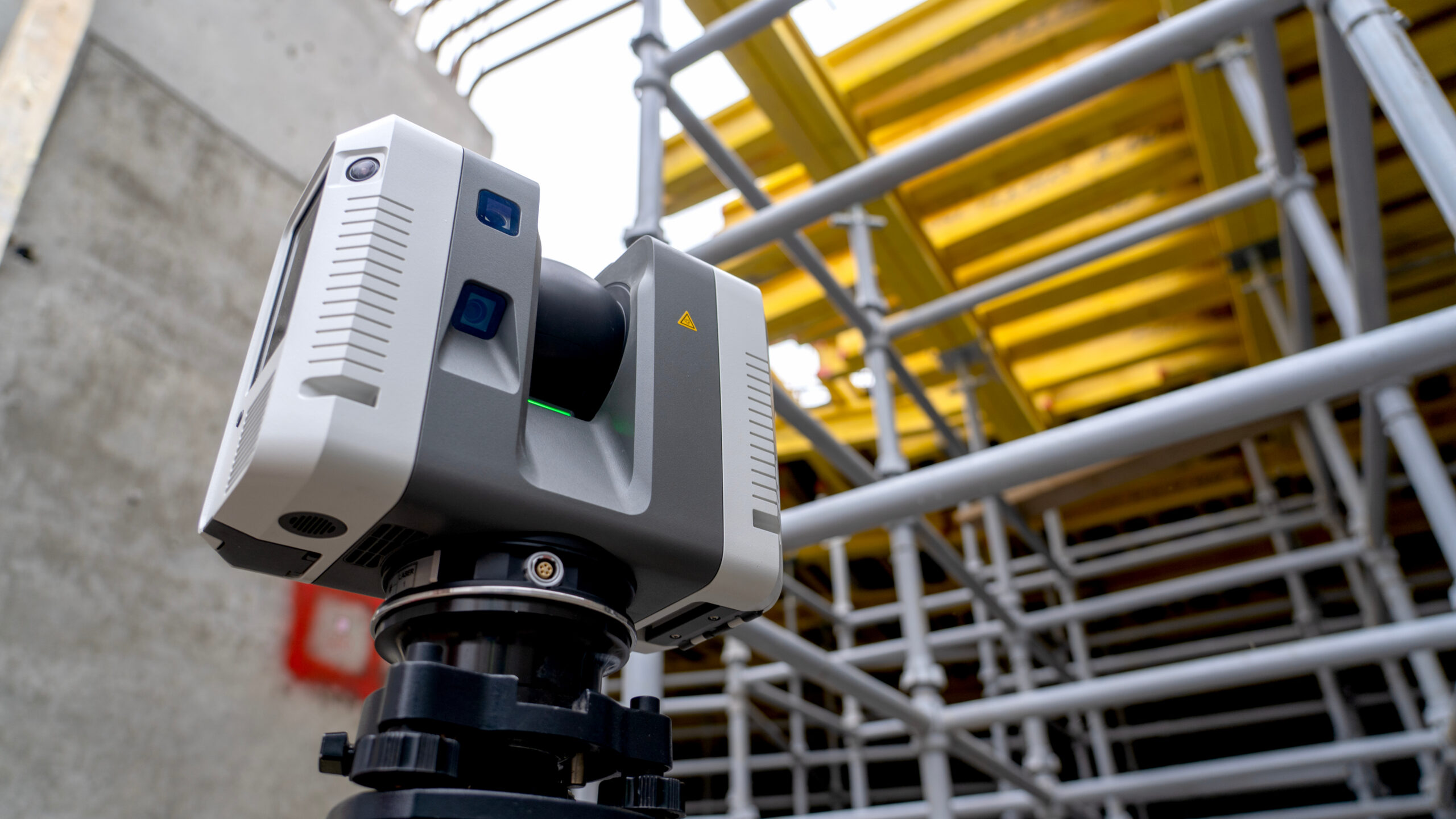 3D laser scanner positioned on an active construction site near scaffolding and concrete structural elements.