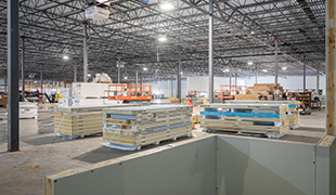 Interior view of a distribution center under construction with structural steel, wall panels, and staged building materials.